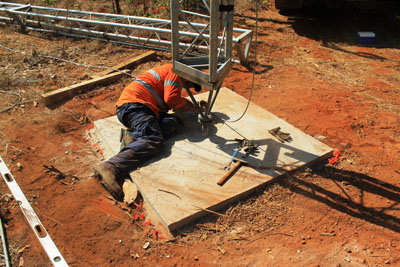 concrete footing of the mast base, with the first section of the mast visible and a rigger lying on the concrete checking the mounting